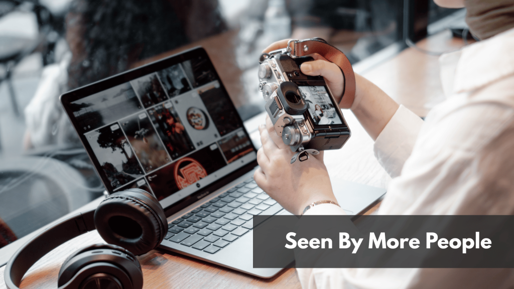 A lady holding a camera while working on her laptop in a desk