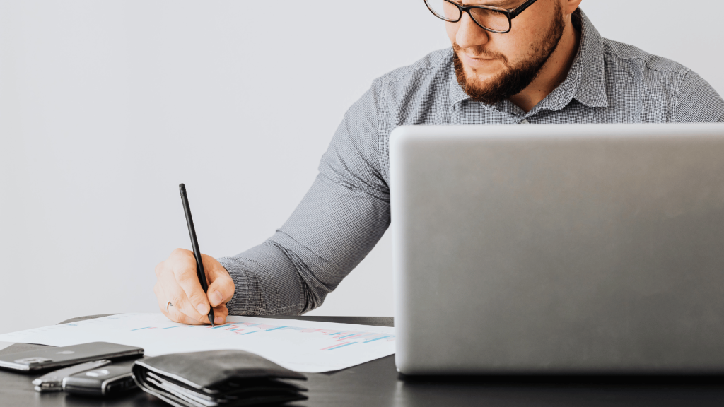Man analyzing marketing charts while working on a laptop, with text overlay 'Analyze and Scale Your Pinterest Strategy'—depicting focused strategy review and data scaling.